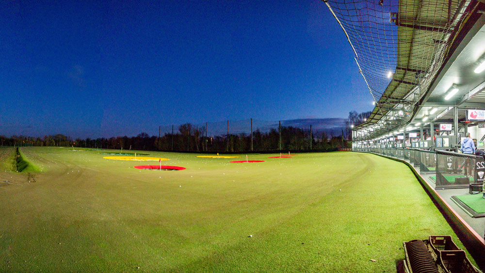 Floodlit golf driving range with illuminated outfield targets at night